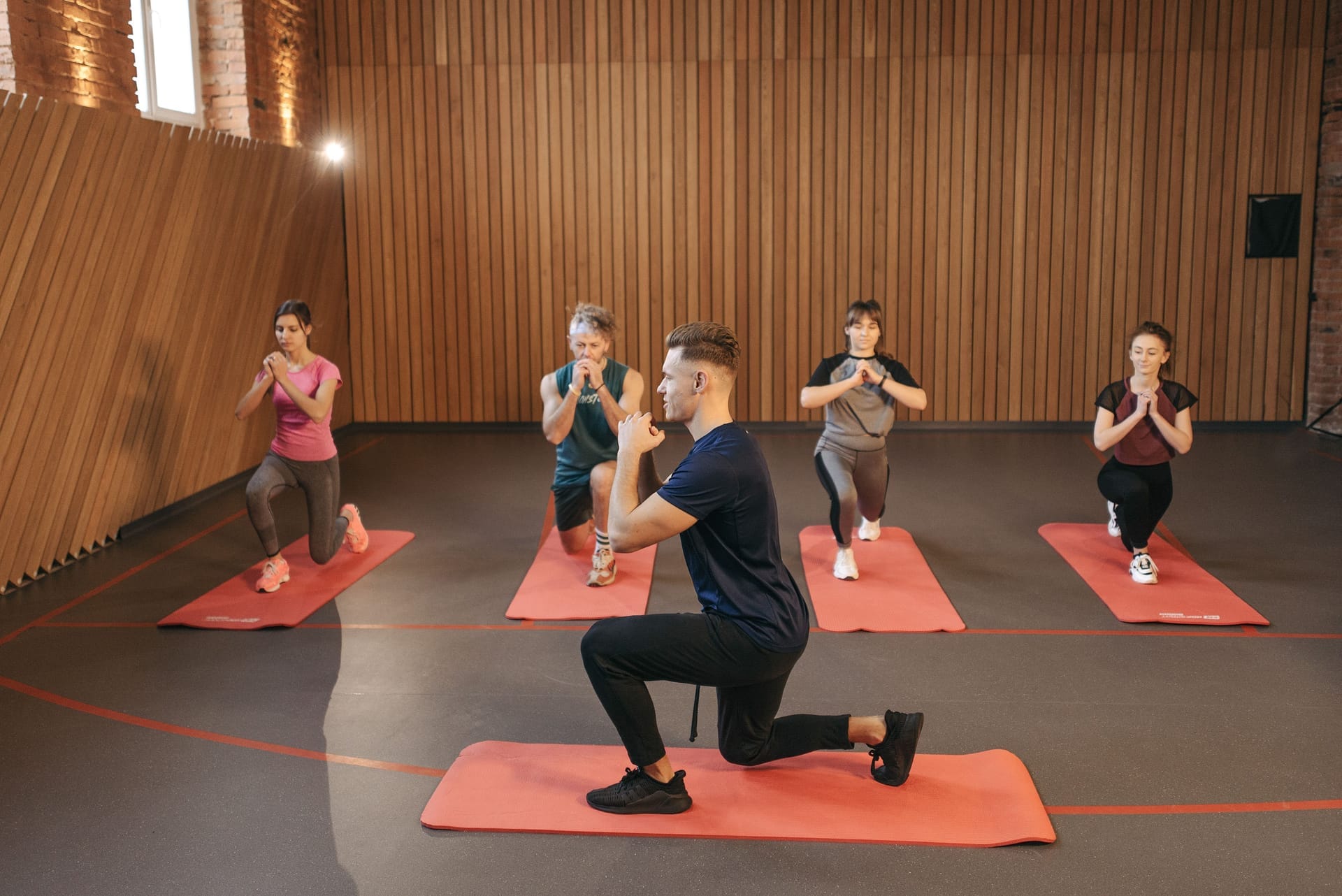 Trainer leading a small group fitness class on mats in a wood-paneled studio