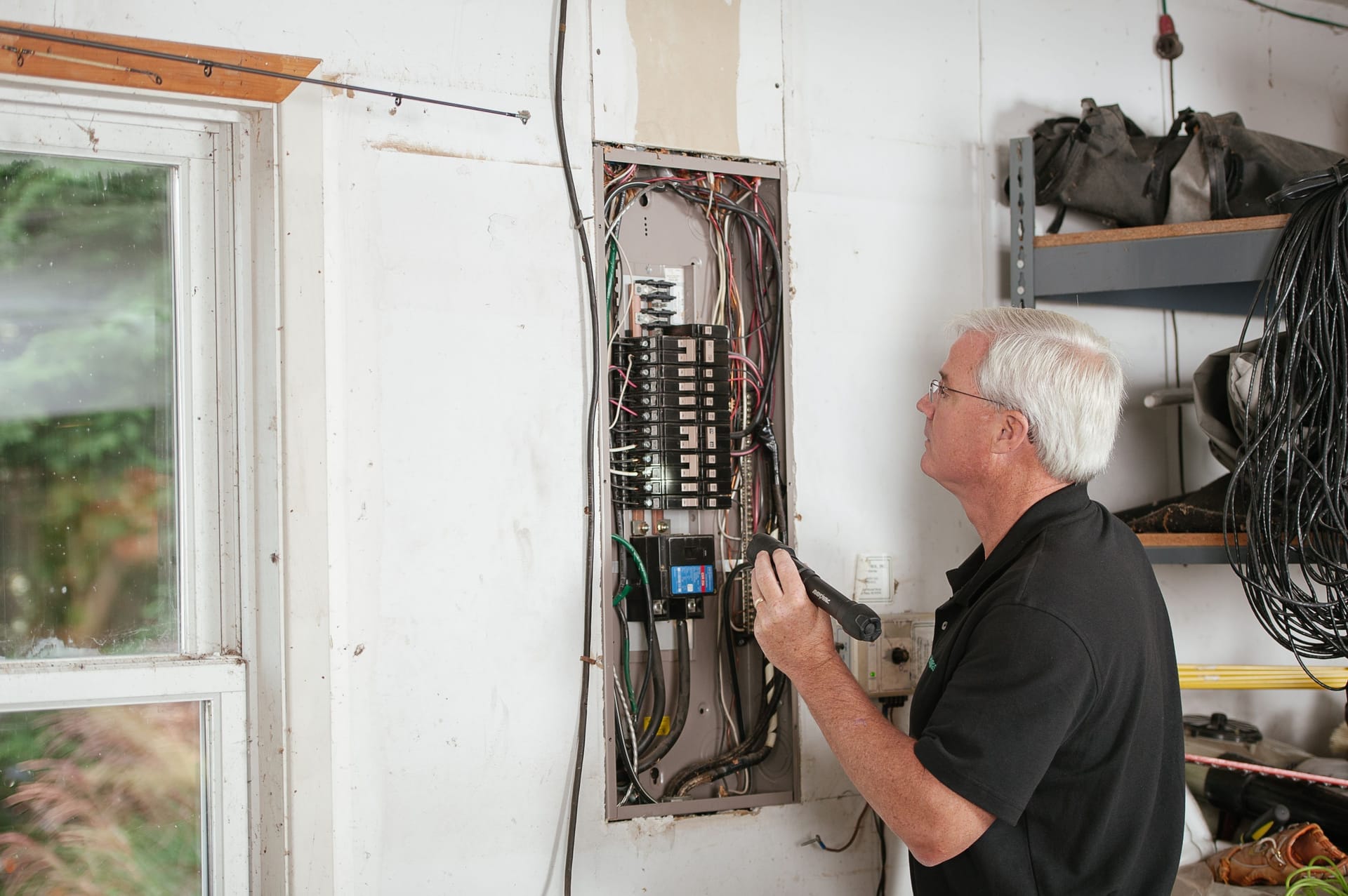 Electrician inspecting a residential breaker panel in a homeowner's garage