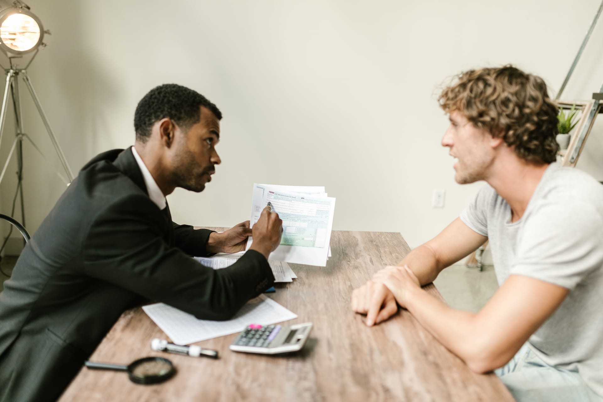Advisor in a suit explaining paperwork to a client across a wooden desk