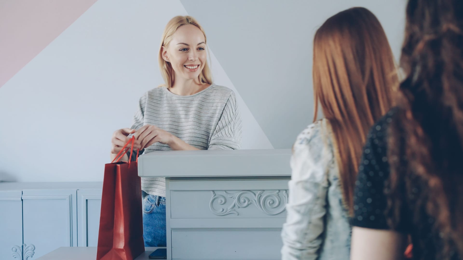 Boutique owner at the checkout counter handing a shopping bag to two customers
